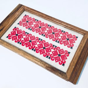 Könnte beinhalten: Ein Holztablett mit einem roten und schwarzen Stickmuster. Die Stickerei zeigt ein sich wiederholendes Muster aus geometrischen Formen.