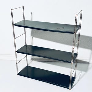 May include: A three-tiered, vintage-style shelf unit. The shelves are a dark, matte black, and the frame is made of twisted metal. The shelves are rectangular and evenly spaced, creating a functional and decorative storage solution.
