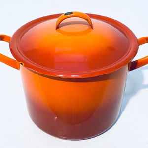 以下が含まれることがあります： オレンジ色のエナメル製の鍋で、ふたが付いていて、持ち手が2つ付いています。鍋はオレンジから赤へのグラデーションになっています。
