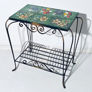 May include: A black metal record stand with a tiled top featuring colourful floral designs. The stand has a shelf for storing records.