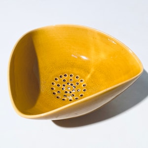 May include: A yellow ceramic colander with a triangular shape and a round hole pattern in the bottom.