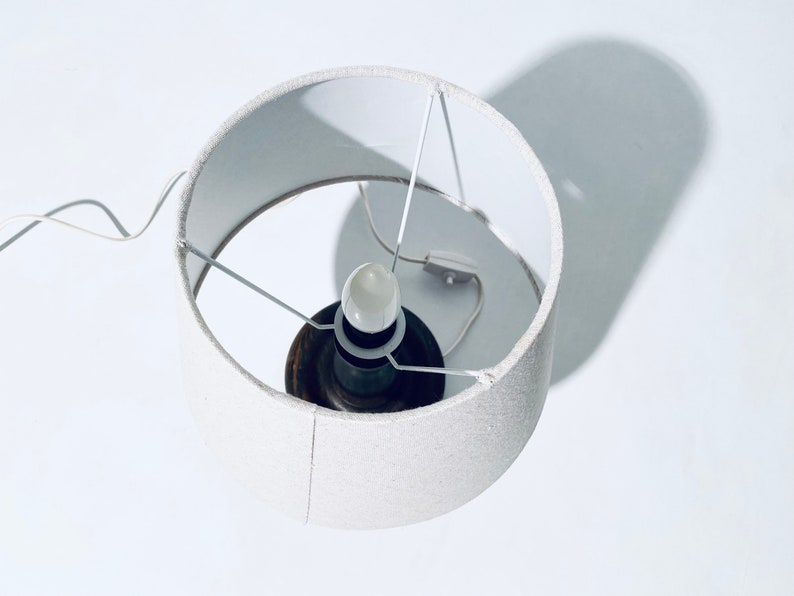 May include: A white lampshade with a white cord and a light bulb inside. The lampshade is made of a textured fabric.