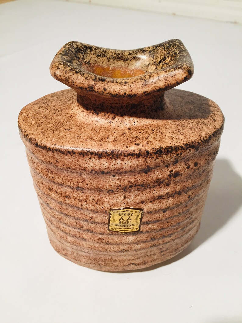 Może przedstawiać: Brązowy ceramiczny wazon z fakturowaną powierzchnią i złotą etykietą z napisem "Vest, Handgefertigt, West Germany".