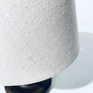 May include: A white linen lampshade with a brown wooden base.