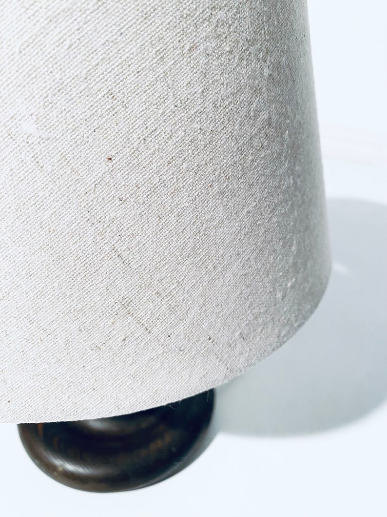 May include: A white linen lampshade with a brown wooden base.