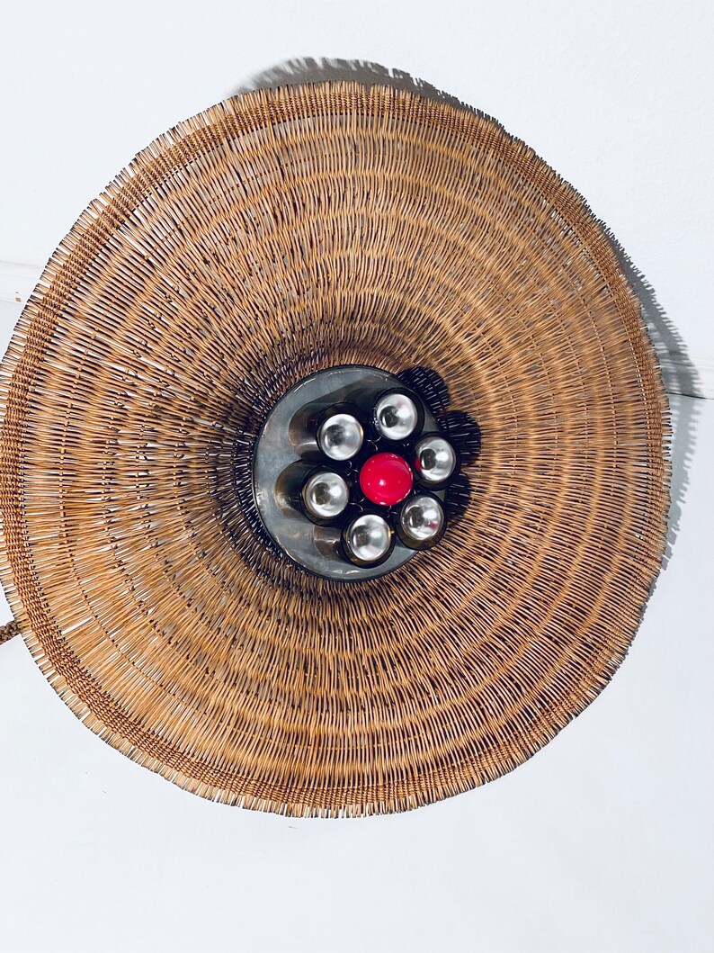 May include: A round, woven wicker lampshade with a metal base and six light bulbs, one of which is red.