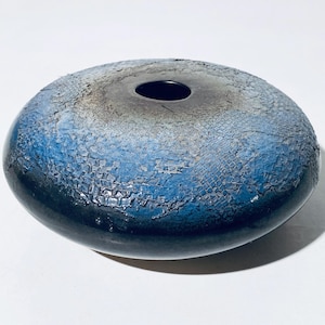 Könnte beinhalten: Eine blaue und schwarze Keramikvase mit einer craquelé-Glasur. Die Vase ist rund und hat eine breite Öffnung.