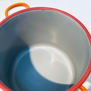 Pu&ograve; includere: Pentola smaltata arancione e rossa con interno grigio. La pentola ha un'unica maniglia sul lato.