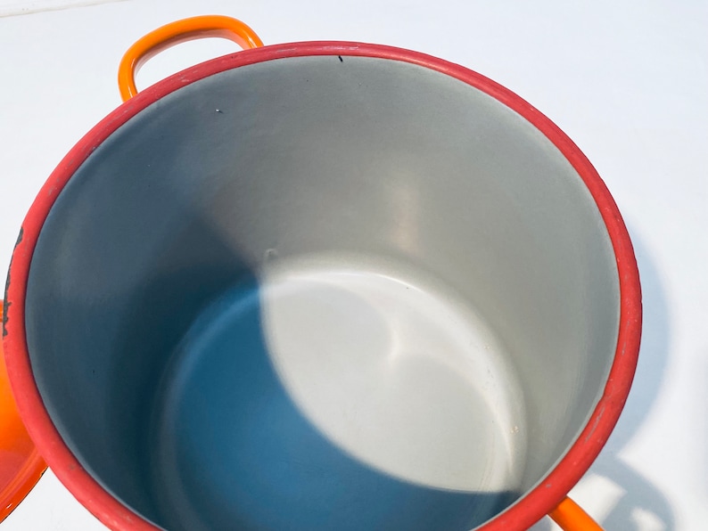 Pu&ograve; includere: Pentola smaltata arancione e rossa con interno grigio. La pentola ha un'unica maniglia sul lato.
