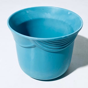 Könnte beinhalten: Ein hellblauer Plastiktopf mit einem dekorativen Design am oberen Rand.