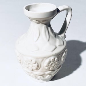 May include: White ceramic pitcher with a floral design. The pitcher has a handle and a rounded body.