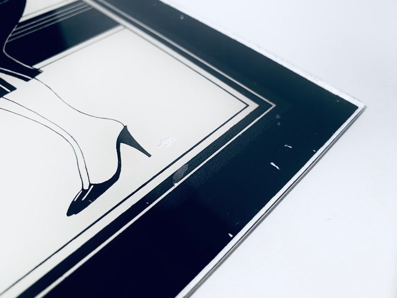 May include: A black and white framed print of a woman's legs in high heels. The print is framed with a black and white border.