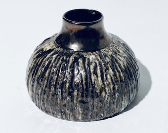 May include: A small, round, ceramic vase with a textured, brown and white glaze. The vase has a wide, round base and a narrow opening at the top.