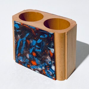 Op de afbeelding: Houten organizer met twee compartimenten, met een kleurrijk abstract ontwerp aan één kant. Het ontwerp is een mix van blauw, oranje, wit en zwart.