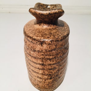 Może przedstawiać: Brązowy ceramiczny wazon z fakturowanym, nakrapianym wykończeniem. Wazon ma szeroki, płaski otw&oacute;r i zaokrąglone ciało.