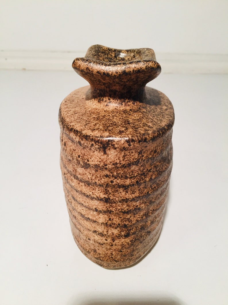 Może przedstawiać: Brązowy ceramiczny wazon z fakturowanym, nakrapianym wykończeniem. Wazon ma szeroki, płaski otw&oacute;r i zaokrąglone ciało.