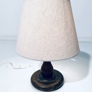 May include: A wooden table lamp with a beige linen lampshade. The lamp has a round wooden base and a wooden stem.