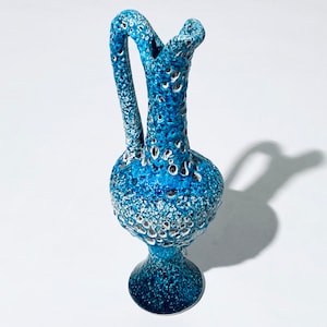 Op de afbeelding: Blauwe keramische kan met een textuur en een handvat. De kan heeft een bolvormig lichaam en een uitlopende voet. Het handvat buigt omhoog en over de bovenkant. De kan is ongeveer 20 cm hoog.