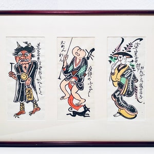Könnte beinhalten: Ein gerahmter Druck von drei japanischen Holzschnitten. Die Drucke sind in Schwarz, Weiß, Rot, Grün und Gelb gehalten. Die Drucke zeigen drei Figuren in traditioneller japanischer Kleidung. Der Text in den Drucken lautet "先えのじど発起して、ねしとえ", "たわんわん", und "座頭のふんどし".