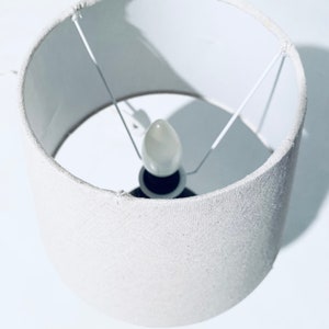 May include: A white fabric lampshade with a white light bulb inside.