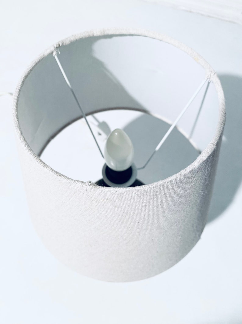 May include: A white fabric lampshade with a white light bulb inside.