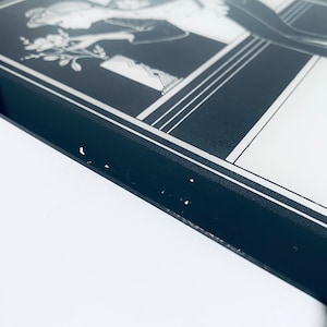 May include: A black and white framed print of a woman in a dress holding a bouquet of flowers. The frame has a silver border.