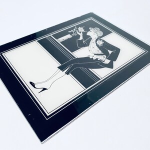 May include: Black and white framed illustration of a woman in a stylish outfit, sitting on a ledge and holding a flower.