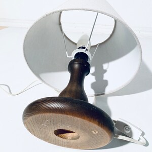 May include: A wooden table lamp with a white fabric lampshade. The lamp has a round base and a brown wooden stem.