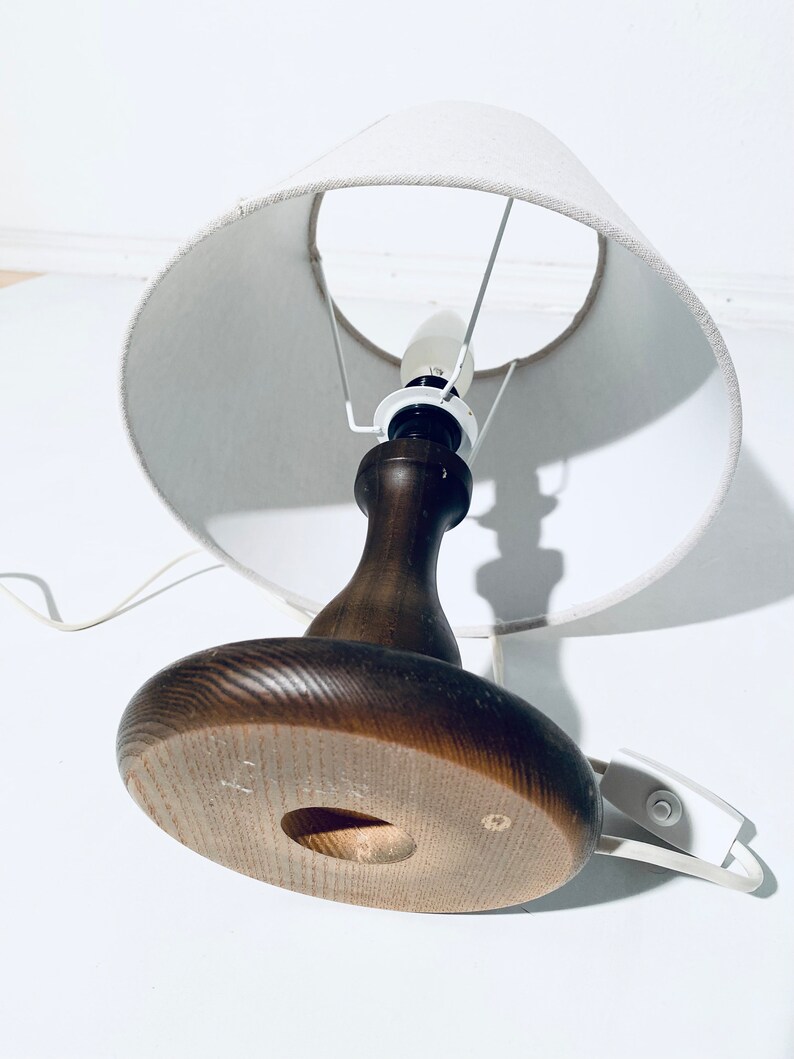 May include: A wooden table lamp with a white fabric lampshade. The lamp has a round base and a brown wooden stem.