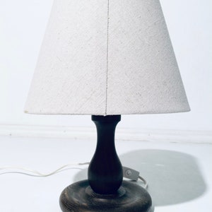 May include: A wooden table lamp with a white fabric lampshade. The lamp has a dark brown wooden base and a round wooden shade.
