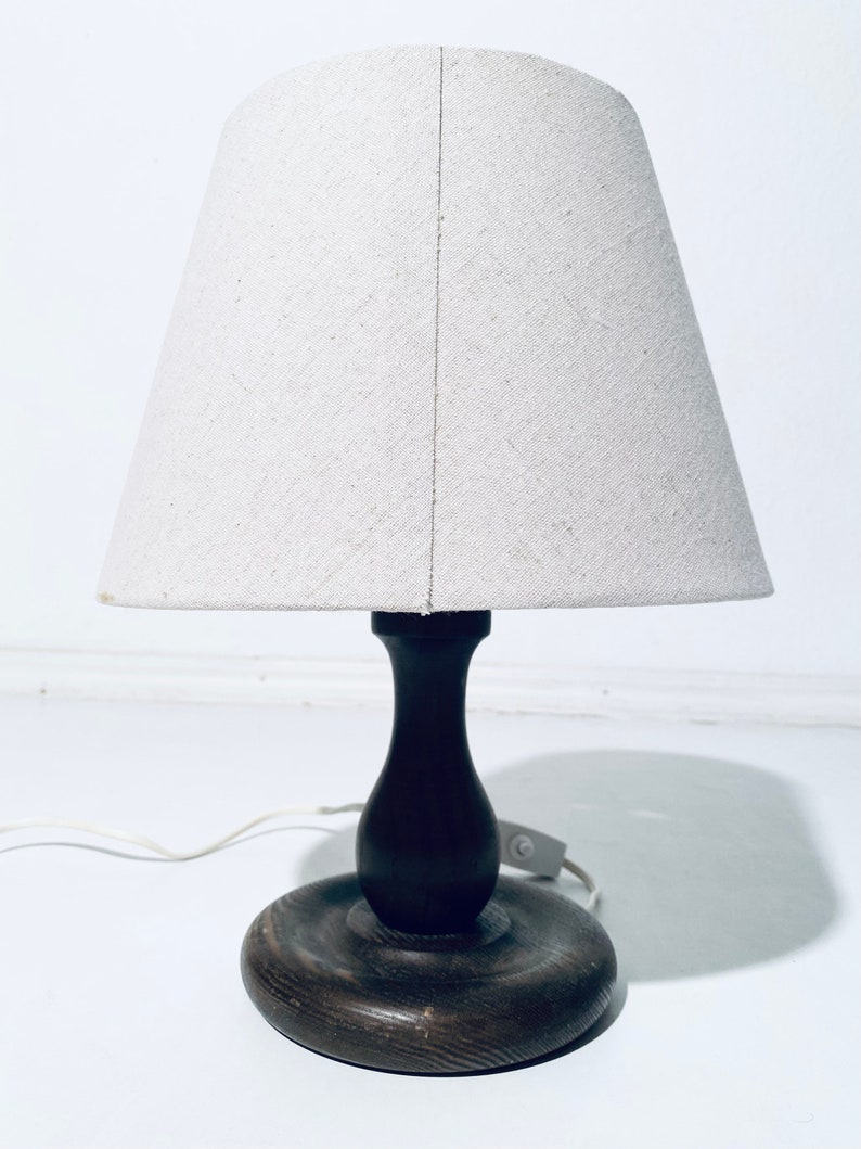 May include: A wooden table lamp with a white fabric lampshade. The lamp has a dark brown wooden base and a round wooden shade.