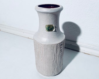 May include: A white ceramic vase with a textured design and a brown rim. The vase has a label that reads "Weston Quality".