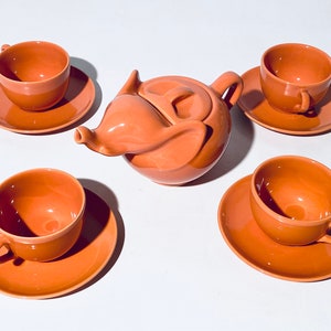 Könnte beinhalten: Eine terracottafarbene Teekanne in Form eines Elefantenkopfes mit vier passenden Teetassen und Untertassen.