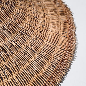 May include: A close-up of a woven, light brown, circular hat made of natural materials. The hat is made of thin, woven strips of material that are tightly packed together.