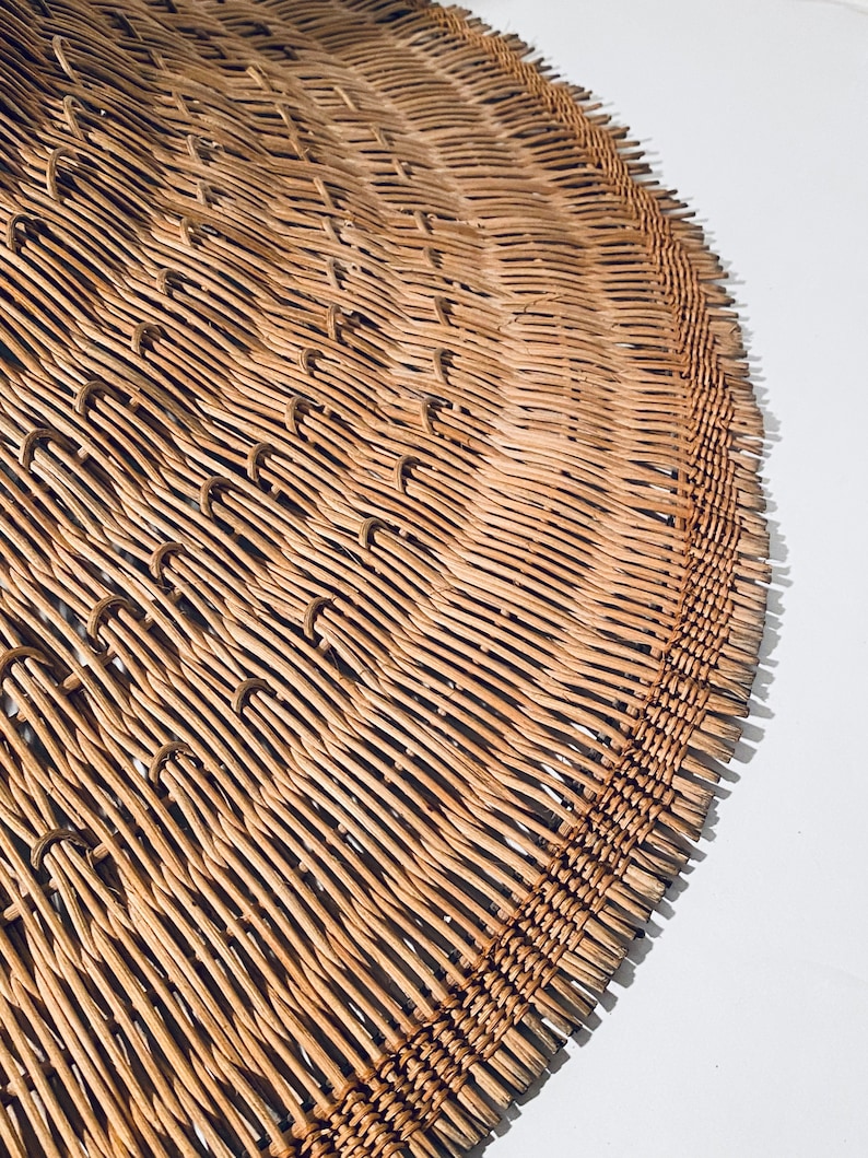 May include: A close-up of a woven, light brown, circular hat made of natural materials. The hat is made of thin, woven strips of material that are tightly packed together.
