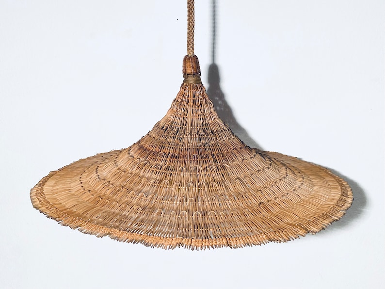 May include: A large, wide-brimmed, conical straw hat with a woven design. The hat is hanging from a cord.