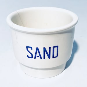 Könnte beinhalten: Ein weißer Keramikbehälter mit einer blauen Aufschrift "SAND".