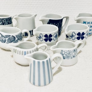 May include: A collection of nine small white ceramic creamer pitchers with blue and white patterns. The patterns include geometric designs, flowers, and stripes.