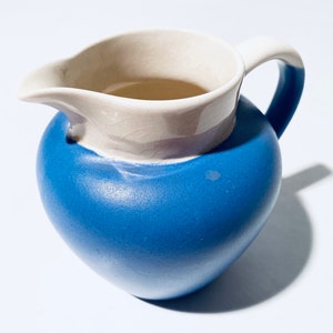 Könnte beinhalten: Eine blaue und weiße Keramikkanne mit rundem Körper und Henkel. Die Kanne hat ein weißes Innenleben und ein blaues Äußeres.