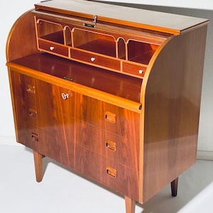Könnte beinhalten: Ein vintage Rolltop-Schreibtisch aus Holz mit einer gewölbten Oberseite und vier Schubladen. Der Schreibtisch hat eine hellbraune Oberfläche und ist aus massivem Holz gefertigt.