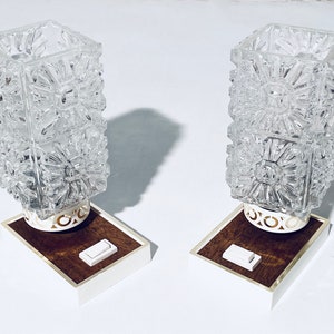 Könnte beinhalten: Zwei Vintage-Tischlampen aus Glas mit geometrischen Mustern. Jede Lampe hat einen weißen Sockel mit einer braunen Holzapplikation und einen weißen Kippschalter.