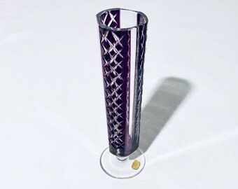 May include: A tall, clear glass vase with a purple, diamond-shaped pattern. The vase has a wide base and a narrow neck.