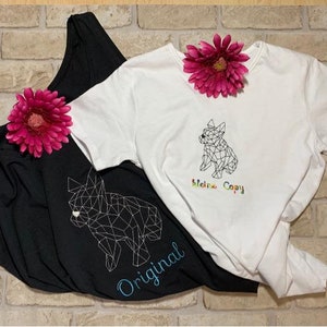 以下が含まれることがあります： 幾何学的な犬のデザインが施された黒と白の2枚のTシャツ。黒いシャツには青で「Original」の文字、白いシャツには虹色で「Meine Copy」の文字が書かれています。ピンクの花がシャツを飾っています。