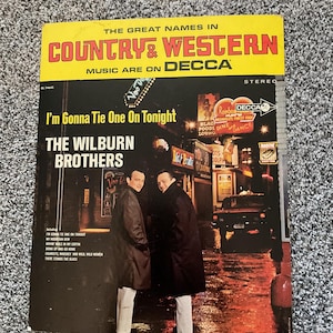 Peut inclure: Une pochette d'album de disque vinyle vintage mettant en scène les frères Wilburn. L'illustration de la pochette représente les frères en manteaux noirs et pantalons blancs debout dans une rue de ville pluvieuse la nuit. Le titre de l'album est "I'm Gonna Tie One On Tonight" et le label est Decca.