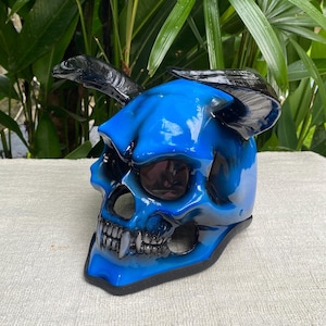 Peut inclure: Un masque de crâne bleu avec des cornes noires. Le masque a une finition brillante avec des ombres bleu foncé et un design squelettique détaillé. Les cornes sont incurvées et noires. Le masque est probablement destiné à un costume ou à des fins décoratives.