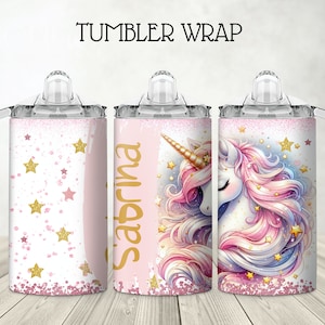 May include: A pink and gold tumbler wrap with a unicorn design and the name "Sabrina" written in gold lettering. The wrap features a unicorn with a pink and blue mane and tail, surrounded by gold stars on a white background.