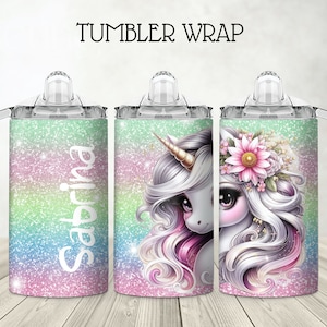 May include: Personalized tumbler wrap with a unicorn design. The unicorn has a pink and white mane and tail, and is wearing a flower crown. The background is a glittery ombre design in shades of pink, blue, and green. The tumbler is clear with a handle and a straw lid. The name "Sabrina" is written on the tumbler.