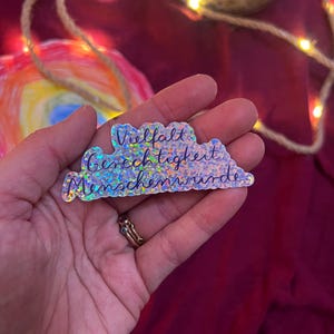 Könnte beinhalten: Ein holografischer Aufkleber in Wolkenform mit dem Text "Vielfalt, Gerechtigkeit, Menschenwürde".