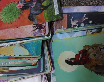 May include: A stack of colorful tarot cards with images of a horse, a woman sitting on a lion, and a woman in the air. The top card has the text "Knight of Air" on it.