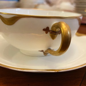 May include: A white teacup and saucer with a gold rim and handle. The cup has a gold design on the side.